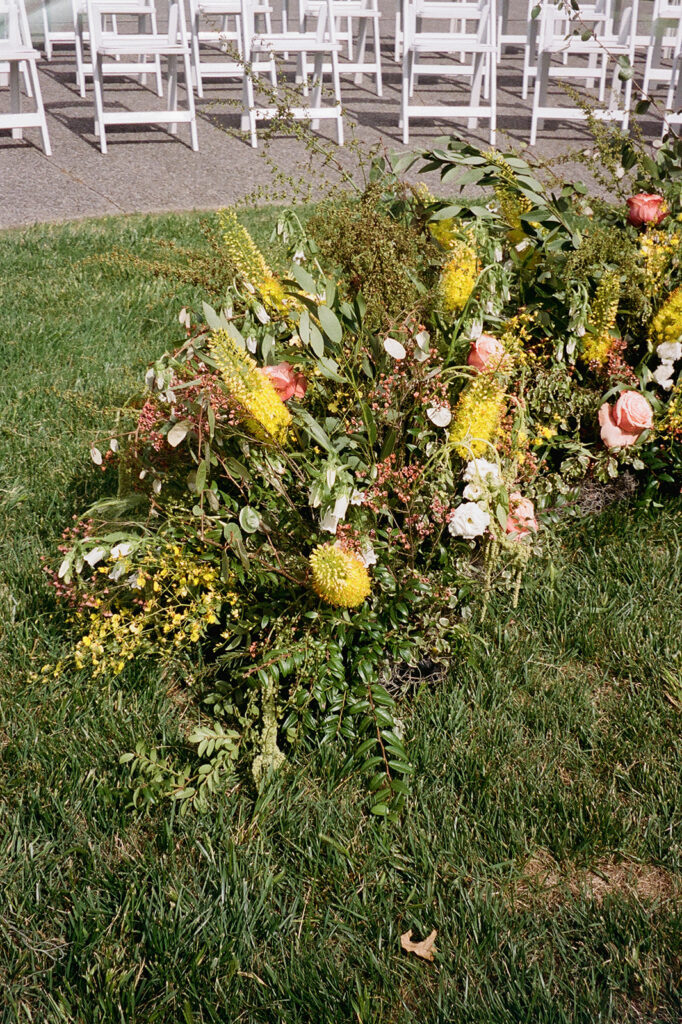 Floral ground meadows for spring wedding ceremony. Unique circle ceremony for outdoor Tennessee wedding. Ceremony floral installation includes a variety of greenery and flowers, with dominant hues of yellow and orange, accented by soft pink and white roses. Unique vibrant spring florals. Design by Rosemary & Finch Floral Design in Nashville, TN.