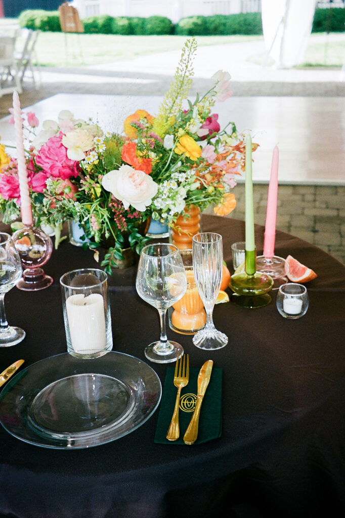 Spring floral centerpieces in bright, cheerful colors, featuring pink peonies, white roses, and wildflowers in orange and yellow. Styled citrus fruits, such as oranges, lemons, limes, and grapefruits for wedding reception tables. Spring wedding with vibrant and unique floral design. Colored glass candle sticks and spiral tapers add unique candle design. Design by Rosemary & Finch Floral Design in Nashville, TN. 