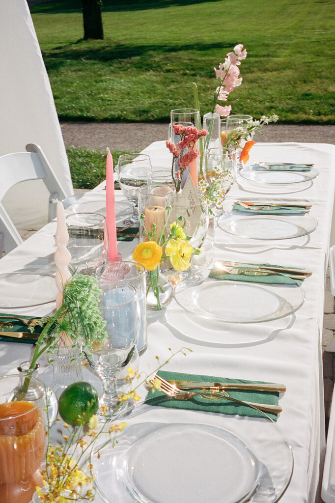 Spring floral centerpieces in bright, cheerful colors, featuring pink peonies, white roses, and wildflowers in orange and yellow. Styled citrus fruits, such as oranges, lemons, limes, and grapefruits for wedding reception tables. Spring wedding with vibrant and unique floral design. Colored glass candle sticks and spiral tapers add unique candle design. Design by Rosemary & Finch Floral Design in Nashville, TN. 