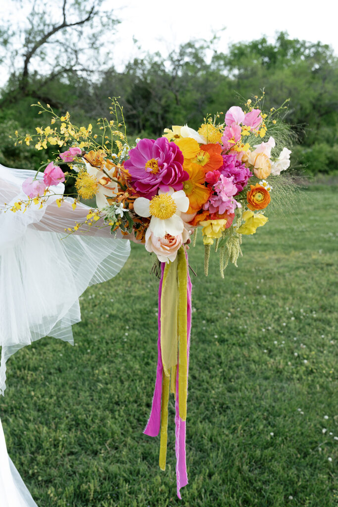 Vibrant and colorful bridal bouquet with flowers that includes lush, fully bloomed peonies in rich magenta, complemented by bright orange and yellow poppies. Summer bridal and bridesmaids’ bouquet with unique and bold spring colors. Whimsical wedding floral with statement making colors. Design by Rosemary & Finch Floral Design. 