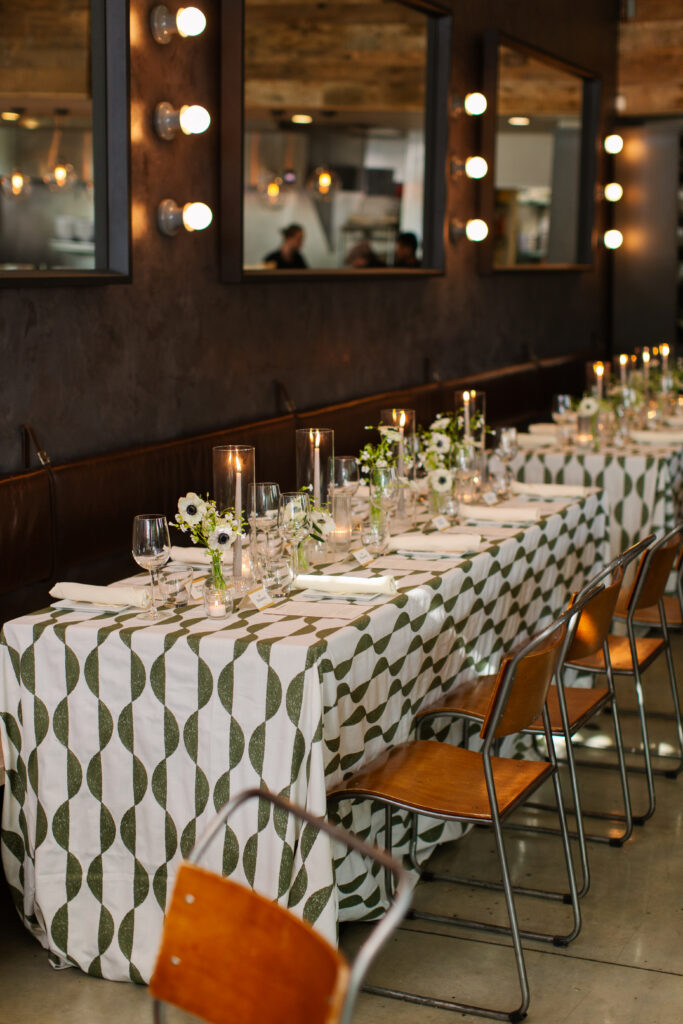 Timeless rehearsal dinner florals in a classic black and white with accents of green color palette. Bud vases and candlelight adorn the tables of this formal rehearsal dinner. Statement urn featuring olive branches and anemones decorate the bar of this reception space. Design by Rosemary & Finch Floral Design in Nashville, TN.