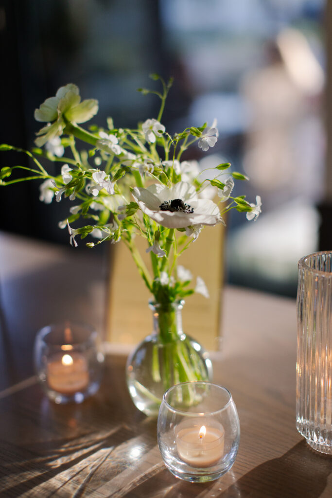 Timeless rehearsal dinner florals in a classic black and white with accents of green color palette. Bud vases and candlelight adorn the tables of this formal rehearsal dinner. Statement urn featuring olive branches and anemones decorate the bar of this reception space. Design by Rosemary & Finch Floral Design in Nashville, TN.