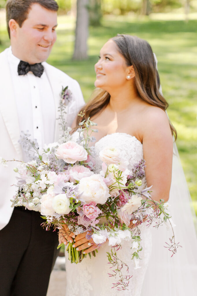 Elegant bridal bouquet in soft pastel colors, including shades of pink, white, and lavender. Mix of roses, peonies, and other delicate blooms, accented with greenery. Lush garden style bridal bouquet for spring wedding. Bridesmaids’ bouquets accenting bridal. Design by Rosemary & Finch Floral Design in Nashville, TN. 