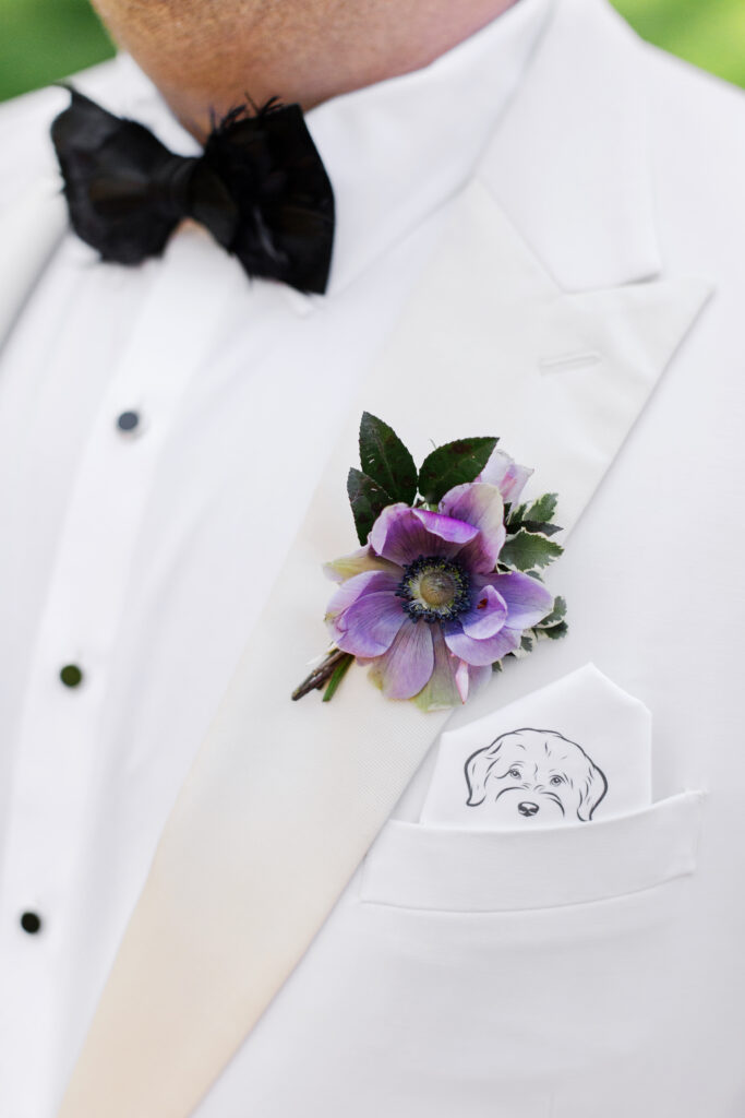 Lavender boutonniere for groom in spring wedding ceremony. Pastel color palette for spring wedding which shades of pink, purple, lavender, and cream. Design elements of cherry tree, blue patterned linens, and custom art. Design by Rosemary & Finch Floral Design in Nashville, TN.