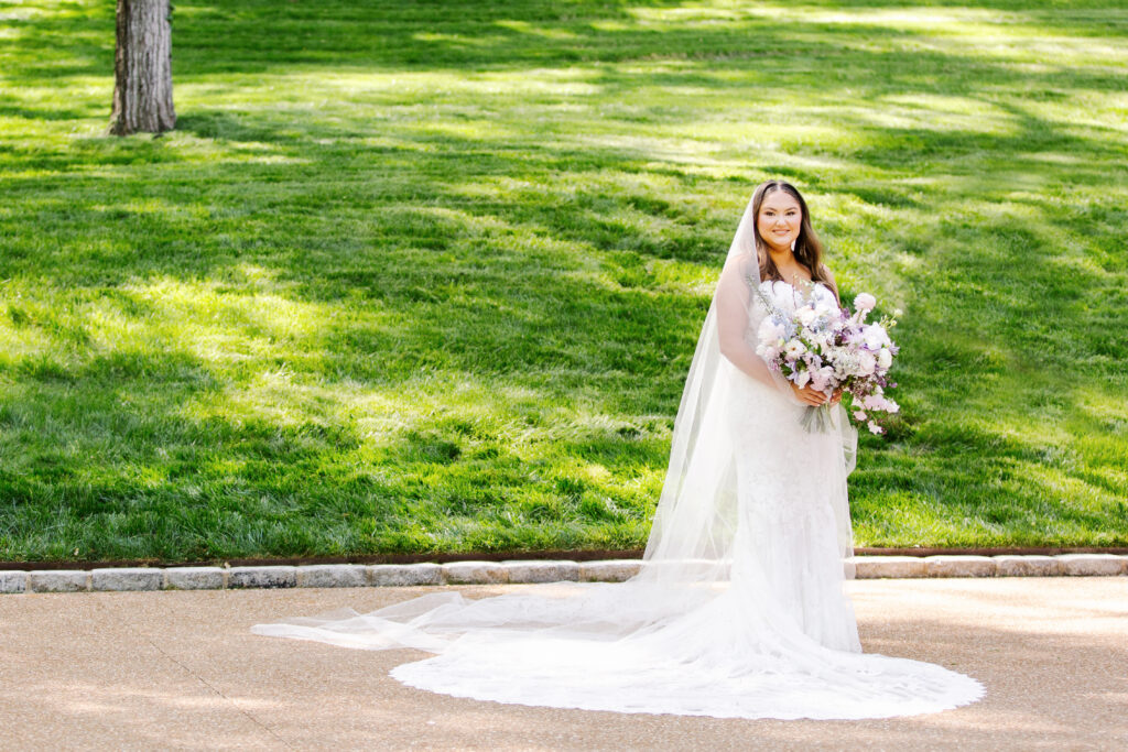 Elegant bridal bouquet in soft pastel colors, including shades of pink, white, and lavender. Mix of roses, peonies, and other delicate blooms, accented with greenery. Lush garden style bridal bouquet for spring wedding. Bridesmaids’ bouquets accenting bridal. Design by Rosemary & Finch Floral Design in Nashville, TN. 