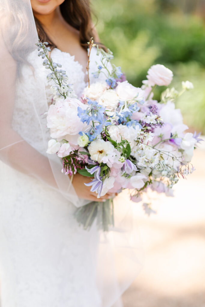 Elegant bridal bouquet in soft pastel colors, including shades of pink, white, and lavender. Mix of roses, peonies, and other delicate blooms, accented with greenery. Lush garden style bridal bouquet for spring wedding. Bridesmaids’ bouquets accenting bridal. Design by Rosemary & Finch Floral Design in Nashville, TN. 