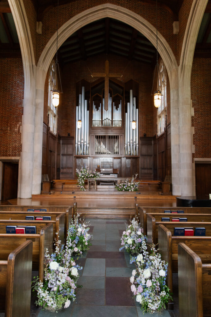 Timeless ceremony floral moments for spring wedding. Church wedding ceremony with wreath adorned doors. Lush and low floral meadows grow to accent the pews and altar of this spring wedding ceremony. Pastel color palette for spring wedding which shades of pink, purple, lavender, and cream. Mix of roses, peonies, and other delicate blooms, accented with greenery. Design by Rosemary & Finch Floral Design. 