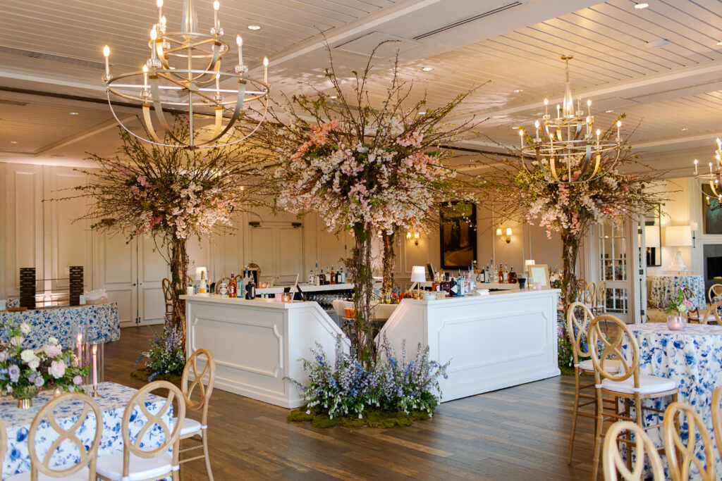 Large cherry trees decorate the reception space of this spring Tennessee wedding reception. Flowering branches and mossy floral meadows add height and interest to this wedding reception bar. Cherry trees for garden-inspired floral design. Pastel color palette for spring wedding which shades of pink, purple, lavender, and cream. Design by Rosemary & Finch Floral Design in Nashville, TN. 