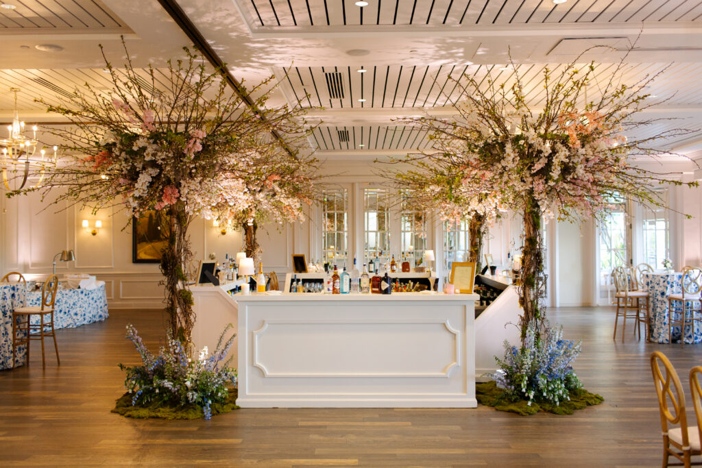 Large cherry trees decorate the reception space of this spring Tennessee wedding reception. Flowering branches and mossy floral meadows add height and interest to this wedding reception bar. Cherry trees for garden-inspired floral design. Pastel color palette for spring wedding which shades of pink, purple, lavender, and cream. Design by Rosemary & Finch Floral Design in Nashville, TN. 