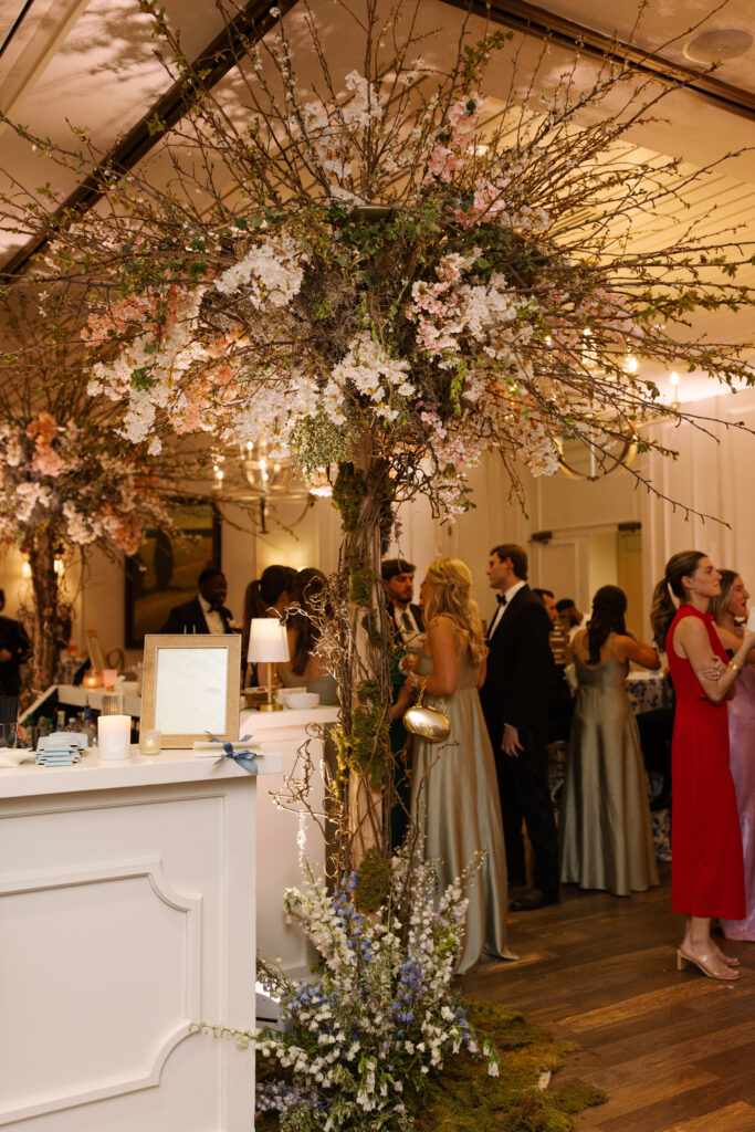 Large cherry trees decorate the reception space of this spring Tennessee wedding reception. Flowering branches and mossy floral meadows add height and interest to this wedding reception bar. Cherry trees for garden-inspired floral design. Pastel color palette for spring wedding which shades of pink, purple, lavender, and cream. Design by Rosemary & Finch Floral Design in Nashville, TN. 