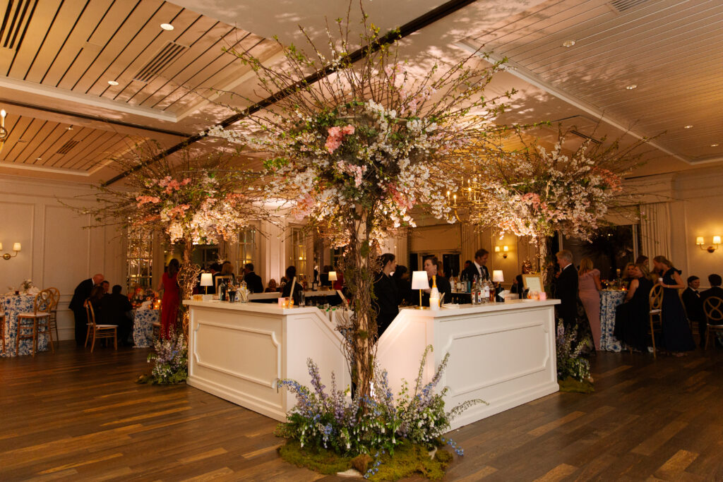 Large cherry trees decorate the reception space of this spring Tennessee wedding reception. Flowering branches and mossy floral meadows add height and interest to this wedding reception bar. Cherry trees for garden-inspired floral design. Pastel color palette for spring wedding which shades of pink, purple, lavender, and cream. Design by Rosemary & Finch Floral Design in Nashville, TN. 