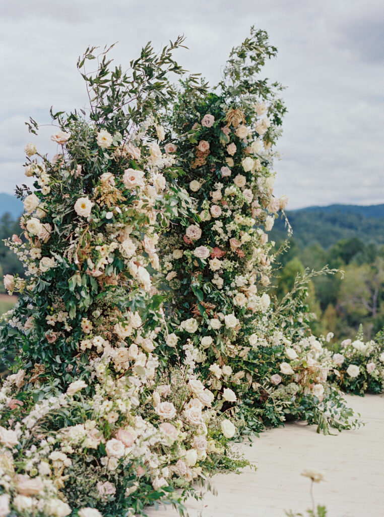 Epic ceremony backdrop for fall wedding at Blackberry Farms. Lush broken arch floral design for wedding ceremony backdrop. Garden inspired growing floral in colors of cream, white, blush, and green. Full coverage floral aisle for wedding ceremony. Floral meadows with petal heavy roses. Floral heavy flora design with elegant and whimsical design. Destination wedding at Blackberry Farm. Design by Rosemary & Finch Floral Design in Nashville, TN. 