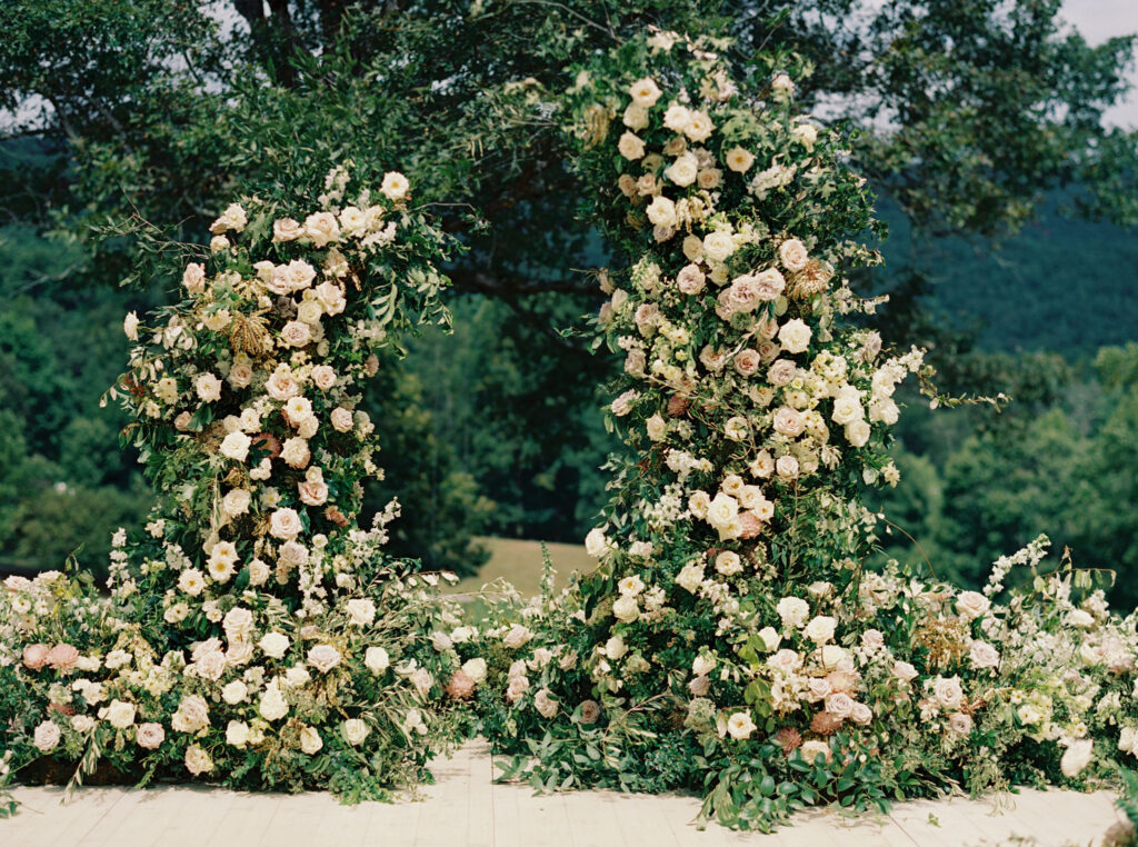 Epic ceremony backdrop for fall wedding at Blackberry Farms. Lush broken arch floral design for wedding ceremony backdrop. Garden inspired growing floral in colors of cream, white, blush, and green. Full coverage floral aisle for wedding ceremony. Floral meadows with petal heavy roses. Floral heavy flora design with elegant and whimsical design. Destination wedding at Blackberry Farm. Design by Rosemary & Finch Floral Design in Nashville, TN. 