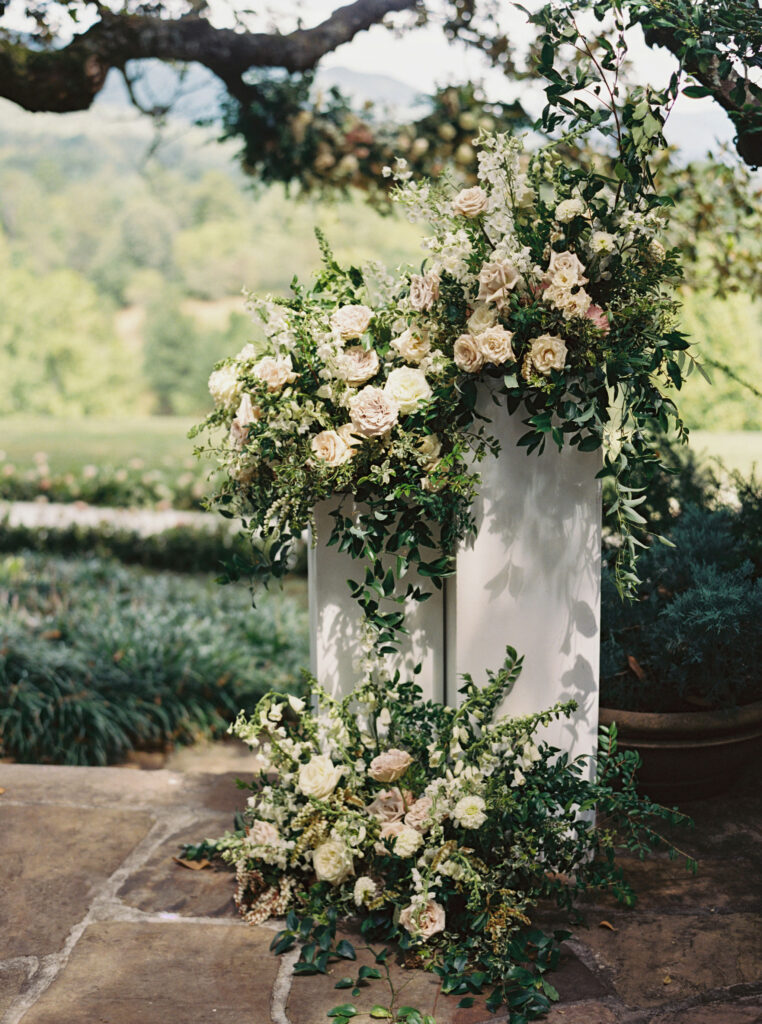 Columns framing the entrance of wedding ceremony aisle adorned with florals. Garden inspired growing floral in colors of cream, white, blush, and green. Growing tree floral installation for fall wedding ceremony. Full coverage floral aisle with whimsical meadow design. Unique wedding ceremony floral design. Fall floral design in timeless white and greens. Destination wedding at Blackberry Farm. Design by Rosemary & Finch Floral Design in Nashville, TN.