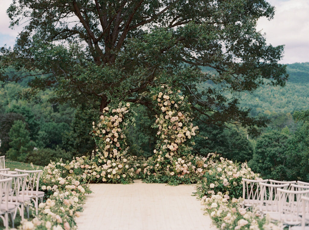 Epic ceremony backdrop for fall wedding at Blackberry Farms. Lush broken arch floral design for wedding ceremony backdrop. Garden inspired growing floral in colors of cream, white, blush, and green. Full coverage floral aisle for wedding ceremony. Floral meadows with petal heavy roses. Floral heavy flora design with elegant and whimsical design. Destination wedding at Blackberry Farm. Design by Rosemary & Finch Floral Design in Nashville, TN. 