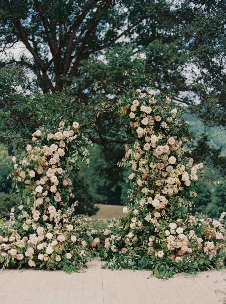 Epic ceremony backdrop for fall wedding at Blackberry Farms. Lush broken arch floral design for wedding ceremony backdrop. Garden inspired growing floral in colors of cream, white, blush, and green. Full coverage floral aisle for wedding ceremony. Floral meadows with petal heavy roses. Floral heavy flora design with elegant and whimsical design. Destination wedding at Blackberry Farm. Design by Rosemary & Finch Floral Design in Nashville, TN. 