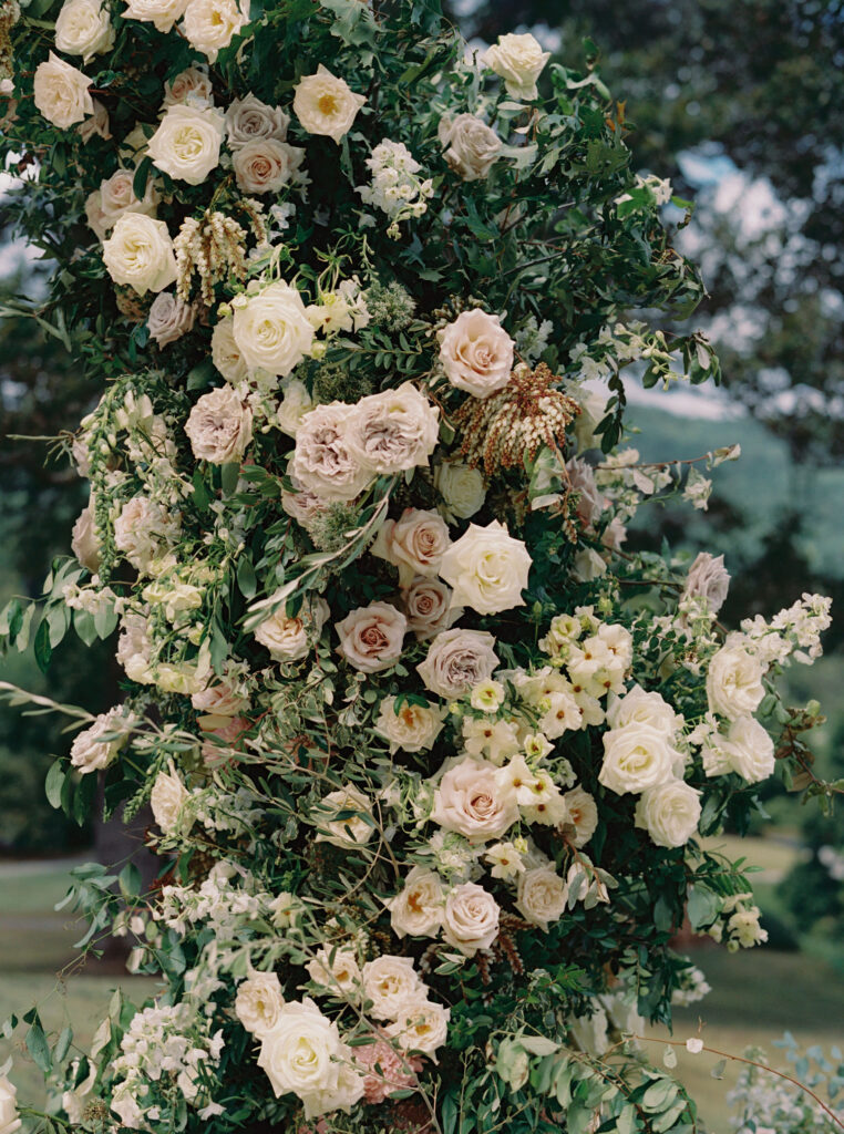 Epic ceremony backdrop for fall wedding at Blackberry Farms. Lush broken arch floral design for wedding ceremony backdrop. Garden inspired growing floral in colors of cream, white, blush, and green. Full coverage floral aisle for wedding ceremony. Floral meadows with petal heavy roses. Floral heavy flora design with elegant and whimsical design. Destination wedding at Blackberry Farm. Design by Rosemary & Finch Floral Design in Nashville, TN. 