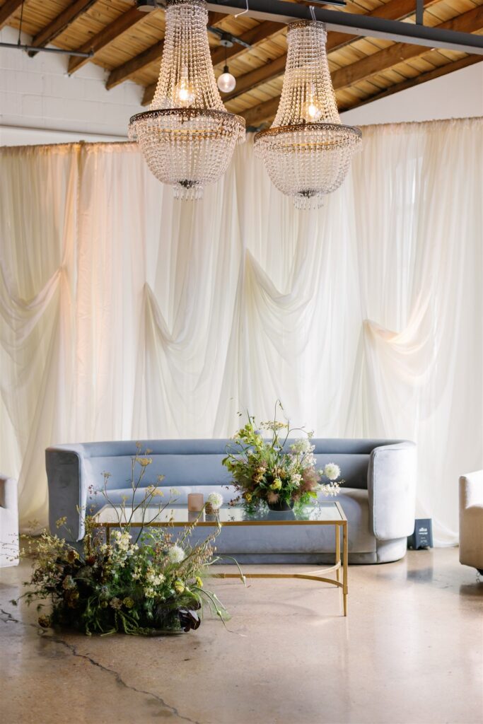 Lush, garden-inspired cocktail hour floral arrangement overflows with texture and movement, featuring Queen Anne’s lace, oncidium orchids, lisianthus, amaranthus, and airy grasses. With earthy greens, soft whites, golden yellow, and touches of mauve and burgundy, the flowers spill naturally, creating a whimsical, meadow-like focal point for a modern lounge setting. Design by Rosemary & Finch Floral Design in Nashville, TN.
