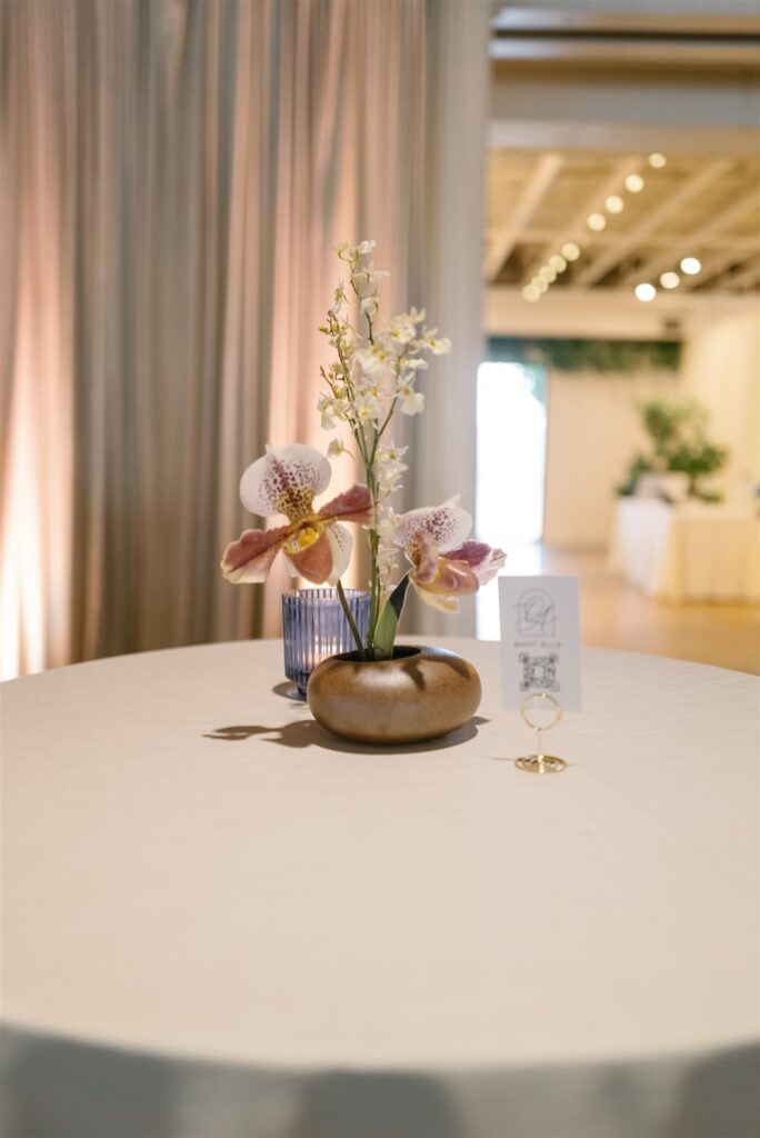 Whimsical and dainty ikebana arrangements are a focal point for cocktail tables at bridal fashion show in Nashville, TN. Arrangements consist of oncidium orchids, slipper orchids, and allium sativum. Colors of soft whites, yellows and burgundy are featured. Design by Rosemary & Finch Floral Design in Nashville, TN.