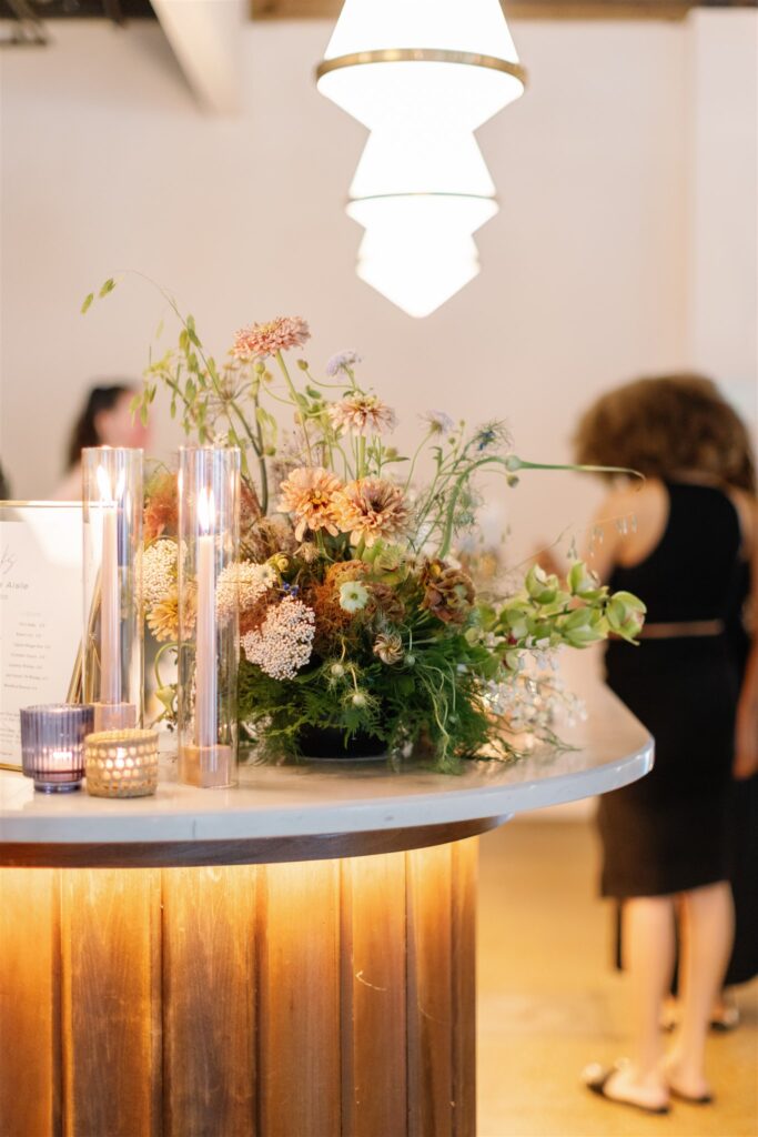 Lush, garden-inspired bar arrangement for bridal fashion show in Nashville, TN. The bar statement features texture and movement, with Queen Anne’s lace, oncidium orchids, lisianthus, zinnias, coneflower, smokebush, forget me nots and airy grasses. With earthy greens, soft whites, golden yellow, mauve and burgundy, the flowers create a whimsical, meadow-like focal point for a modern bar. Design by Rosemary & Finch Floral Design in Nashville, TN.