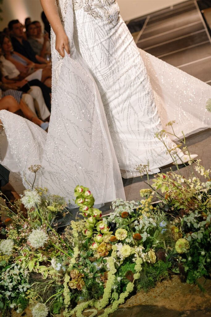 Garden-inspired, whimsical arrangements for bridal fashion show in Nashville, TN. Floral arrangements feature texture and movement, with Queen Anne’s lace, oncidium orchids, blue nigella, lisianthus, zinnias, amaranthus, allium, coneflower, smokebush, forget me nots and airy grasses. With earthy greens, soft whites, golden yellow, mauve and burgundy, the flowers spill out and showcase a meadow-like focal point for a fashion runway. Design by Rosemary & Finch Floral Design in Nashville, TN.