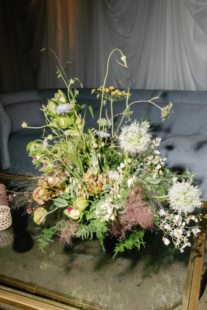 Lush, garden-inspired florals for summer bridal fashion show in Nashville, TN. Textured floral arrangements consist of Queen Anne’s lace, oncidium orchids, blue nigella, lisianthus, zinnias, amaranthus, allium, coneflower, smokebush, forget me nots, ferns and airy grasses. With earthy greens, soft whites, yellows, mauve and burgundy, the flowers spill out and showcase a modern and editorial focal point for bridal portraits. Design by Rosemary & Finch Floral Design in Nashville, TN.