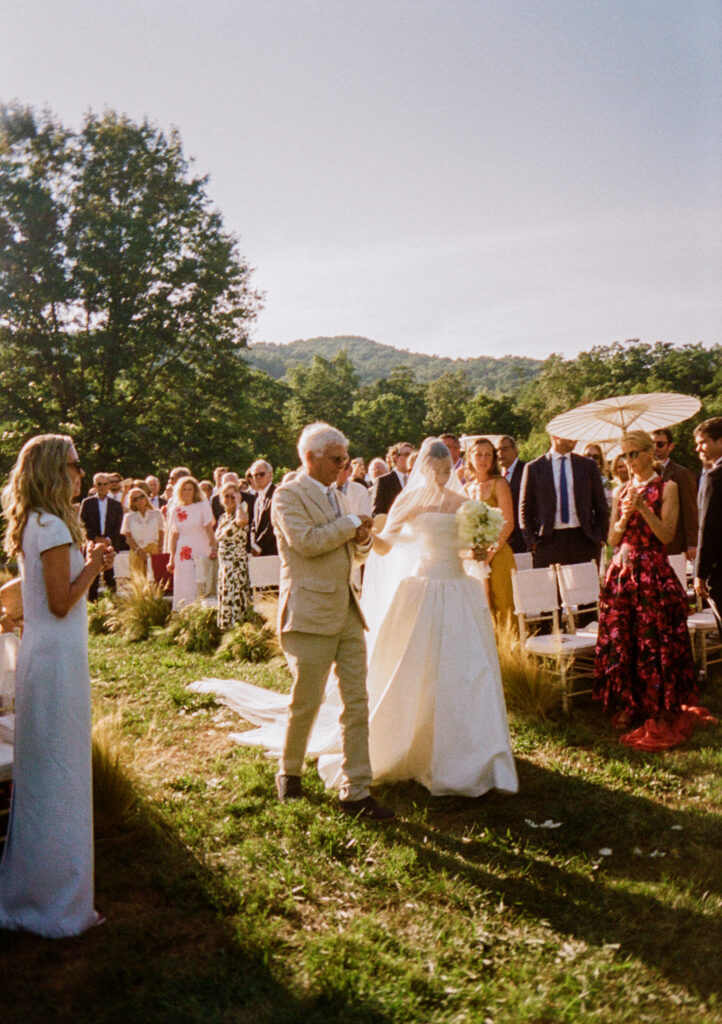 Elegant, organic and untamed outdoor wedding ceremony at Blackberry Farms featured in Vogue. Whimsical, grassy meadows line the aisle and floral accents are highlighted with white cosmos, green mist, solidago, yarrow, scabiosa and grasses. Pergola is covered in lush greenery with soft touches of cream roses and wispy meadows at the base. Design by Rosemary & Finch Floral Design in Nashville, TN. 