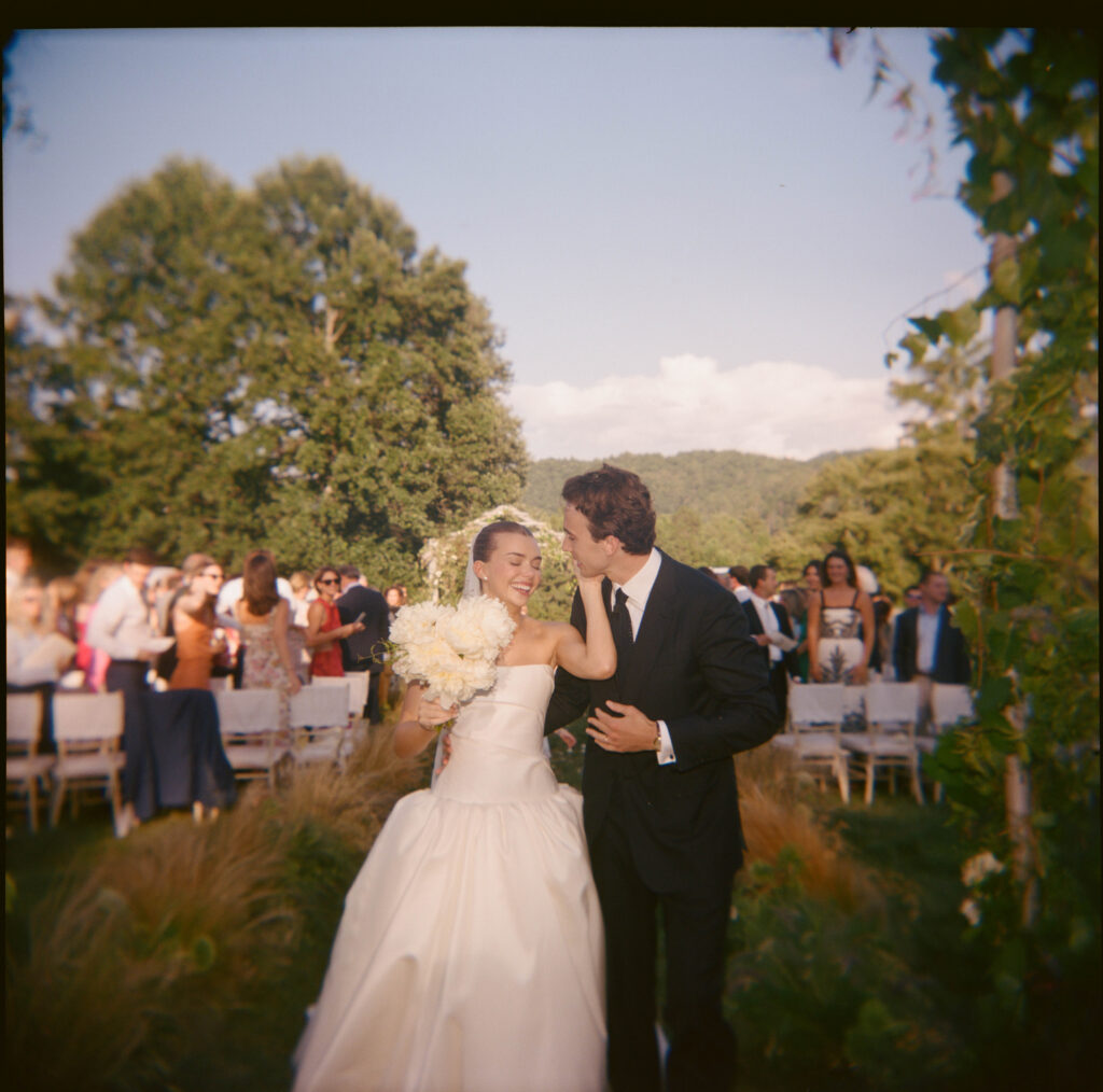Elegant, organic and untamed outdoor wedding ceremony at Blackberry Farms featured in Vogue. Whimsical, grassy meadows line the aisle and floral accents are highlighted with white cosmos, green mist, solidago, yarrow, scabiosa and grasses. Pergola is covered in lush greenery with soft touches of cream roses and wispy meadows at the base. Design by Rosemary & Finch Floral Design in Nashville, TN. 