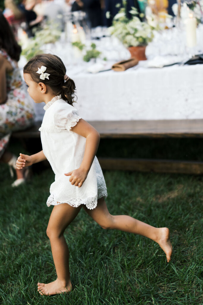 Romantic and timeless outdoor garden wedding reception featured in Vogue at Blackberry Farms. The floral design highlights white seasonal wildflowers such as cosmos, Queen Anne’s lace, sweet peas, clematis, and saponaria, with touches of texture including flowering smokebush, maidenhair fern, and herbs for a garden-inspired style atop lace table linens. Warm candlelight and soft tones create a sophisticated and intimate atmosphere. Design by Rosemary & Finch Floral Design in Nashville, TN.