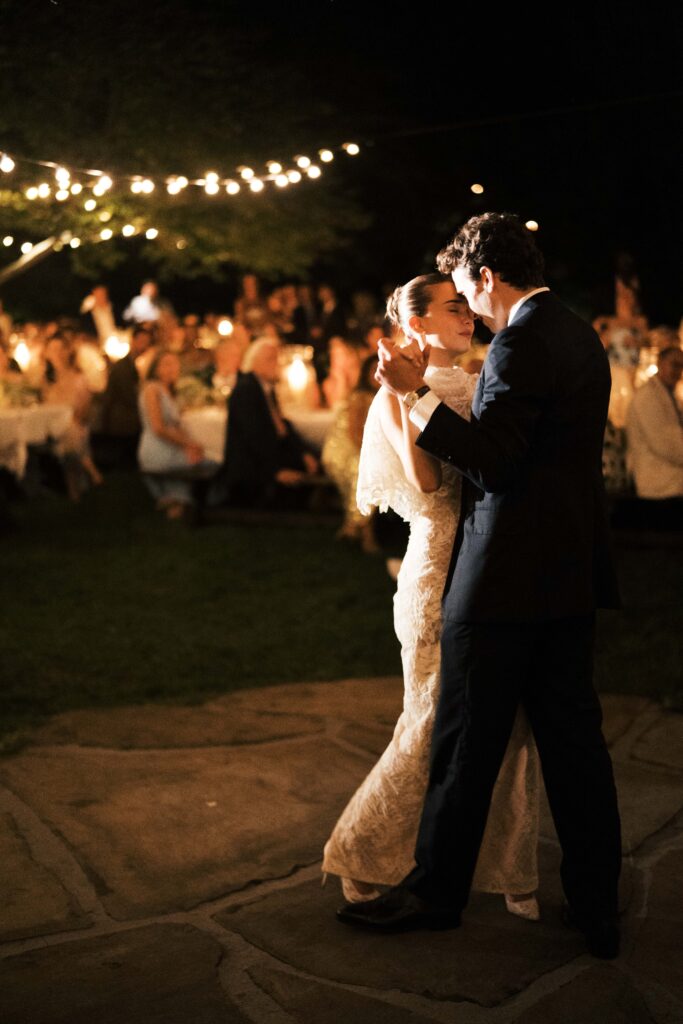 Romantic and timeless outdoor garden wedding reception featured in Vogue at Blackberry Farms. The floral design highlights white seasonal wildflowers such as cosmos, Queen Anne’s lace, sweet peas, clematis, and saponaria, with touches of texture including flowering smokebush, maidenhair fern, and herbs for a garden-inspired style atop lace table linens. Warm candlelight and soft tones create a sophisticated and intimate atmosphere. Design by Rosemary & Finch Floral Design in Nashville, TN.