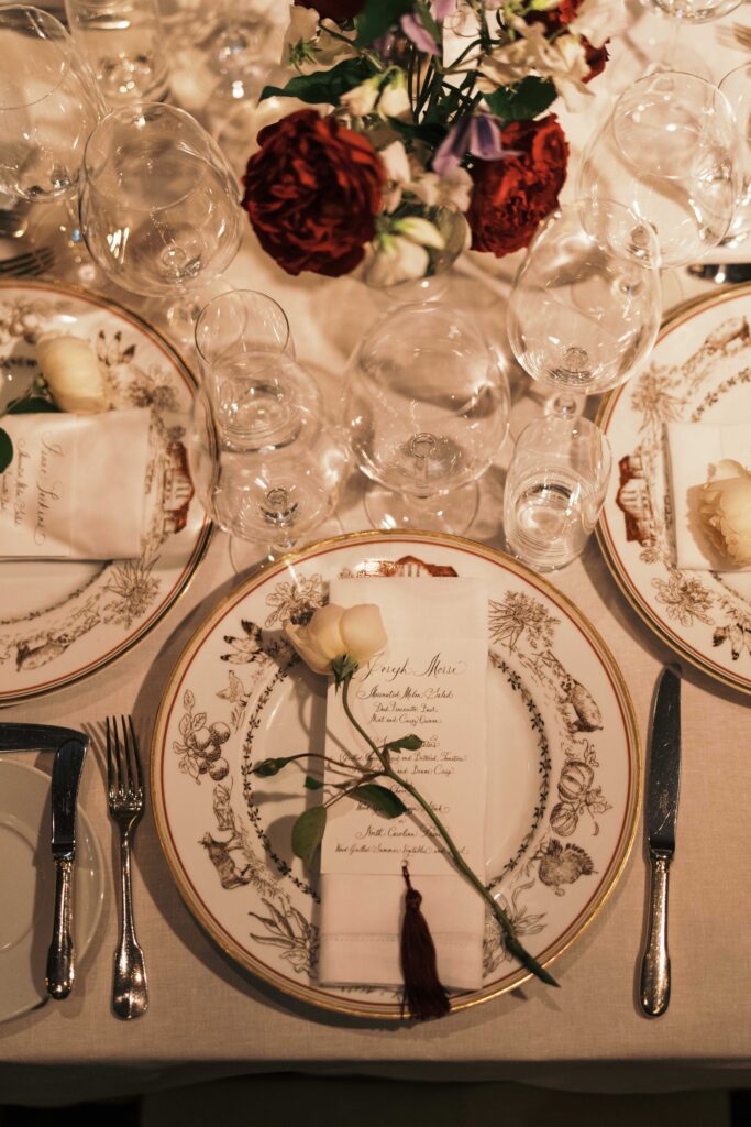 Dark, moody and untamed wedding reception in the barn at Blackberry Farms as featured in Vogue. Hues of deep red, rosy pink, and champagne are featured and florals are composed of garden roses, spray roses, ranunculus, calla lilies, astilbe, sanguisorba, butterfly ranunculus, cornflowers, sweet pea vines, and creeping buttercups with dark greens. Styled fruits and candelabras are centerpieces on tables. Design by Rosemary & Finch Floral Design in Nashville, TN.