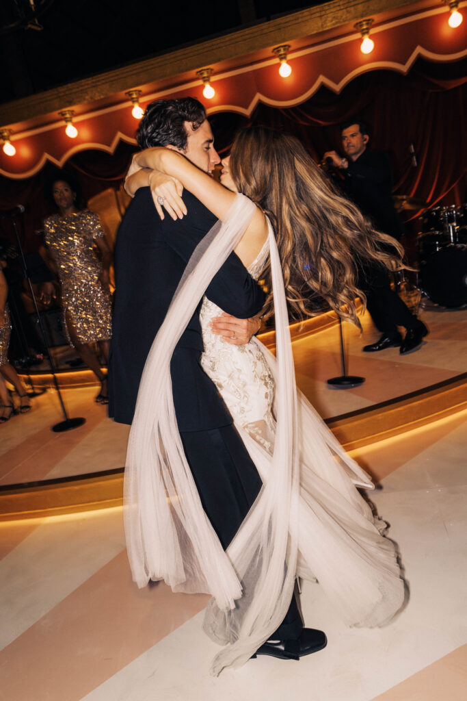 Dark, moody and untamed wedding reception in the barn at Blackberry Farms as featured in Vogue. Hues of deep red, rosy pink, and champagne are featured and florals are composed of garden roses, spray roses, ranunculus, calla lilies, astilbe, sanguisorba, butterfly ranunculus, cornflowers, sweet pea vines, and creeping buttercups with dark greens. Styled fruits and candelabras are centerpieces on tables. Design by Rosemary & Finch Floral Design in Nashville, TN.