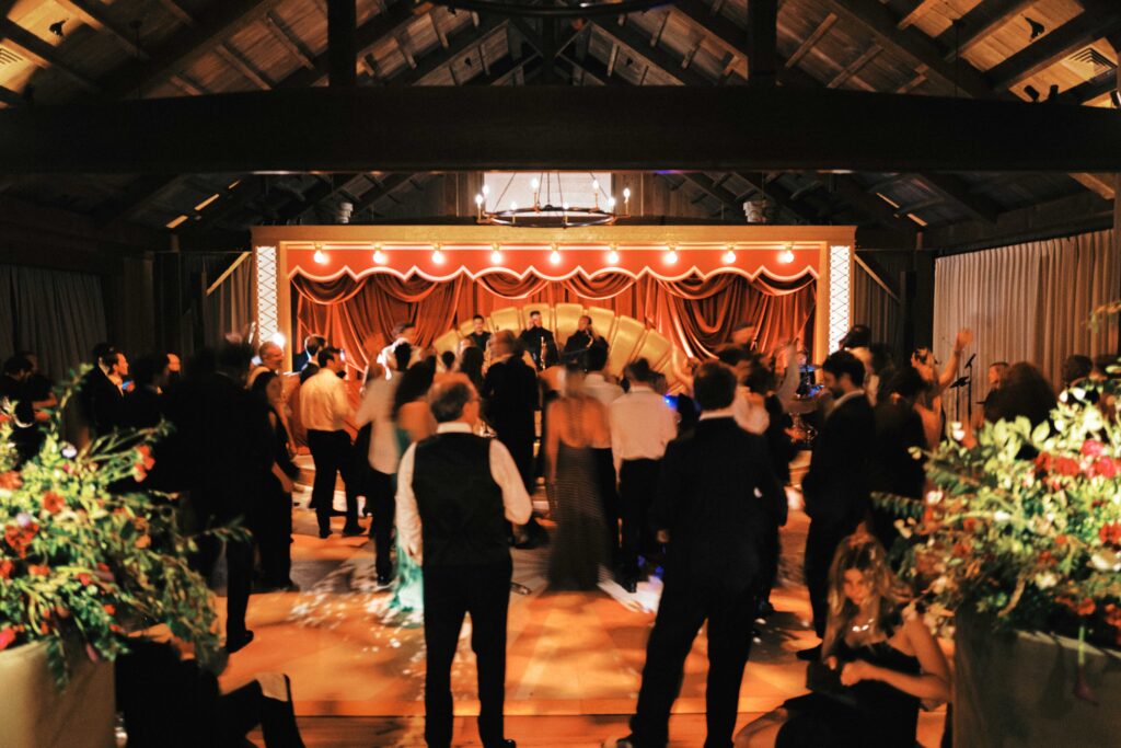Dark, moody and untamed wedding reception in the barn at Blackberry Farms as featured in Vogue. Hues of deep red, rosy pink, and champagne are featured and florals are composed of garden roses, spray roses, ranunculus, calla lilies, astilbe, sanguisorba, butterfly ranunculus, cornflowers, sweet pea vines, and creeping buttercups with dark greens. Styled fruits and candelabras are centerpieces on tables. Design by Rosemary & Finch Floral Design in Nashville, TN.
