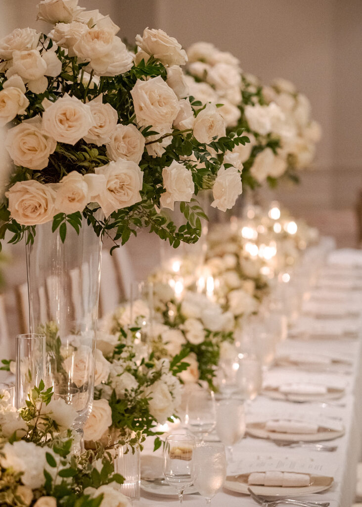 Stunning reception florals for summer wedding reception in Buckhead, Atlanta. All-white floral centerpieces featuring cloud roses, playa blanca roses, peonies, ranunculus, double tulips and lisianthus. Minimal greenery complements beautiful floral table arrangements and bud vases. Elevated all-white rose centerpieces scattered throughout reception. Design by Rosemary & Finch Floral Design in Nashville, TN.