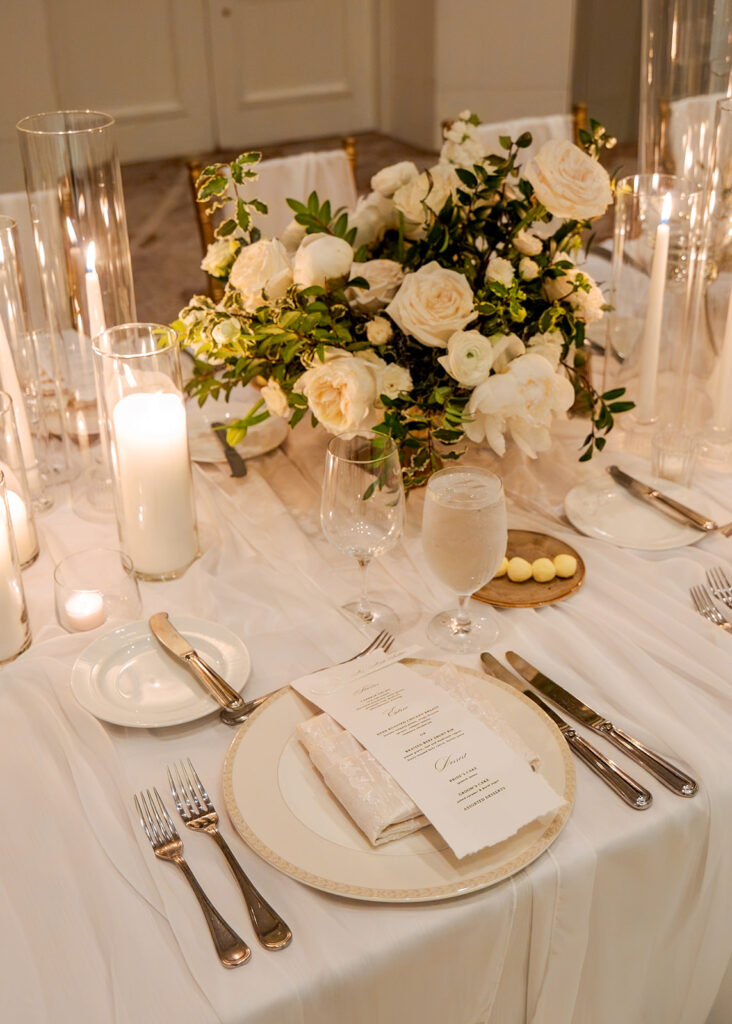 Stunning reception florals for summer wedding reception in Buckhead, Atlanta. All-white floral centerpieces featuring cloud roses, playa blanca roses, peonies, ranunculus, double tulips and lisianthus. Minimal greenery complements beautiful floral table arrangements and bud vases. Elevated all-white rose centerpieces scattered throughout reception. Design by Rosemary & Finch Floral Design in Nashville, TN.