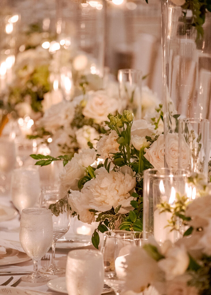 Stunning reception florals for summer wedding reception in Buckhead, Atlanta. All-white floral centerpieces featuring cloud roses, playa blanca roses, peonies, ranunculus, double tulips and lisianthus. Minimal greenery complements beautiful floral table arrangements and bud vases. Elevated all-white rose centerpieces scattered throughout reception. Design by Rosemary & Finch Floral Design in Nashville, TN.