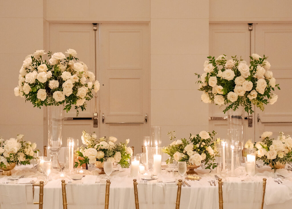 Stunning reception florals for summer wedding reception in Buckhead, Atlanta. All-white floral centerpieces featuring cloud roses, playa blanca roses, peonies, ranunculus, double tulips and lisianthus. Minimal greenery complements beautiful floral table arrangements and bud vases. Elevated all-white rose centerpieces scattered throughout reception. Design by Rosemary & Finch Floral Design in Nashville, TN.