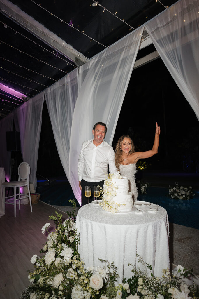 Luxurious, all-white flowers cascading over a stunning wedding cake. Flowers featured are roses, ranunculus, oncidium, delphinium, spray roses and waxflower with a slight amount of greenery. The cake is surrounded by all-white, lush meadows placed on the floor. Meadows include cake flowers as well as lisianthus, hydrangeas, baby’s breath, tulips, mums and more. Design by Rosemary & Finch Floral Design in Nashville, TN. 