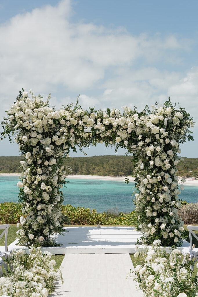 Lush and romantic ceremony chuppah florals for beachfront wedding in the Bahamas. The chuppah highlights garden roses, hydrangeas, delphinium, spray roses, baby’s breath, chrysanthemums, oncidium, wisteria, tulips and a mixture of airy greens to create an elegant and dramatic focal point. Layered textures and soft movement blend seamlessly with lush aisle meadows featuring the same flowers as the chuppah. Design by Rosemary & Finch Floral Design in Nashville, TN.