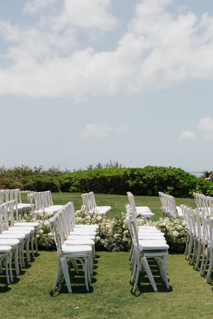 Lush white ceremony florals for a beachfront wedding in the Bahamas featuring garden roses, hydrangeas, delphinium, spray roses, baby’s breath, chrysanthemums, waxflower, carnations, tulips and a mixture of greens to create a refined and romantic aisle arrangement. Layered textures and soft movement give these all-white flowers an elevated, editorial look. Design by Rosemary & Finch Floral Design in Nashville, TN.