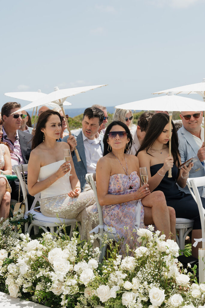 Lush white ceremony florals for a beachfront wedding in the Bahamas featuring garden roses, hydrangeas, delphinium, spray roses, baby’s breath, chrysanthemums, waxflower, carnations, tulips and a mixture of greens to create a refined and romantic aisle arrangement. Layered textures and soft movement give these all-white flowers an elevated, editorial look. Design by Rosemary & Finch Floral Design in Nashville, TN.