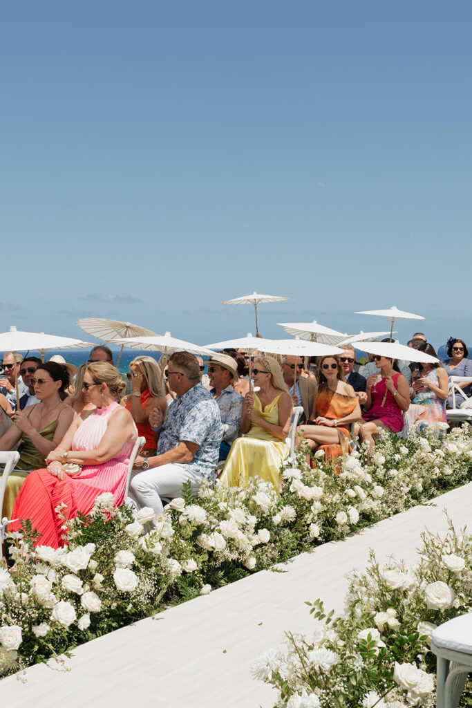Lush white ceremony florals for a beachfront wedding in the Bahamas featuring garden roses, hydrangeas, delphinium, spray roses, baby’s breath, chrysanthemums, waxflower, carnations, tulips and a mixture of greens to create a refined and romantic aisle arrangement. Layered textures and soft movement give these all-white flowers an elevated, editorial look. Design by Rosemary & Finch Floral Design in Nashville, TN.