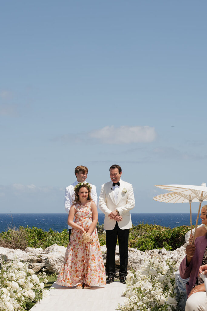 Lush white ceremony florals for a beachfront wedding in the Bahamas featuring garden roses, hydrangeas, delphinium, spray roses, baby’s breath, chrysanthemums, waxflower, carnations, tulips and a mixture of greens to create a refined and romantic aisle arrangement. Layered textures and soft movement give these all-white flowers an elevated, editorial look. Design by Rosemary & Finch Floral Design in Nashville, TN.
