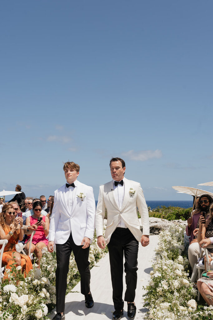 Lush white ceremony florals for a beachfront wedding in the Bahamas featuring garden roses, hydrangeas, delphinium, spray roses, baby’s breath, chrysanthemums, waxflower, carnations, tulips and a mixture of greens to create a refined and romantic aisle arrangement. Layered textures and soft movement give these all-white flowers an elevated, editorial look. Design by Rosemary & Finch Floral Design in Nashville, TN.