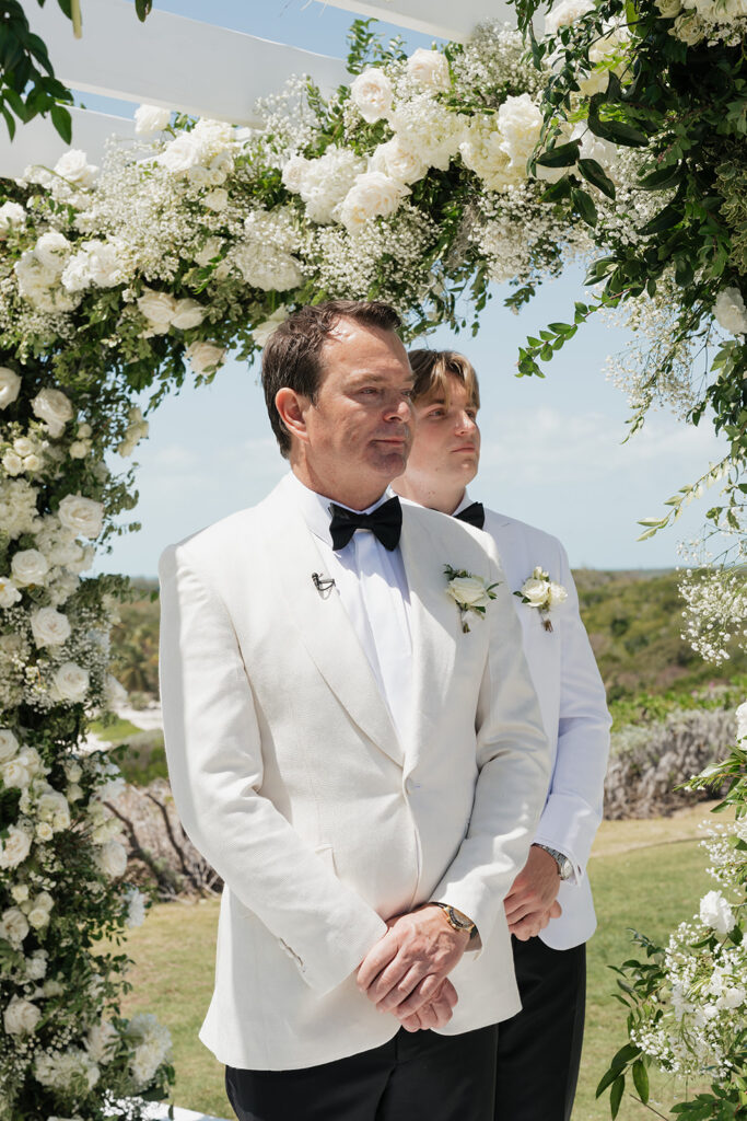 Lush and romantic ceremony chuppah florals for beachfront wedding in the Bahamas. The chuppah highlights garden roses, hydrangeas, delphinium, spray roses, baby’s breath, chrysanthemums, oncidium, wisteria, tulips and a mixture of airy greens to create an elegant and dramatic focal point. Layered textures and soft movement blend seamlessly with lush aisle meadows featuring the same flowers as the chuppah. Design by Rosemary & Finch Floral Design in Nashville, TN.