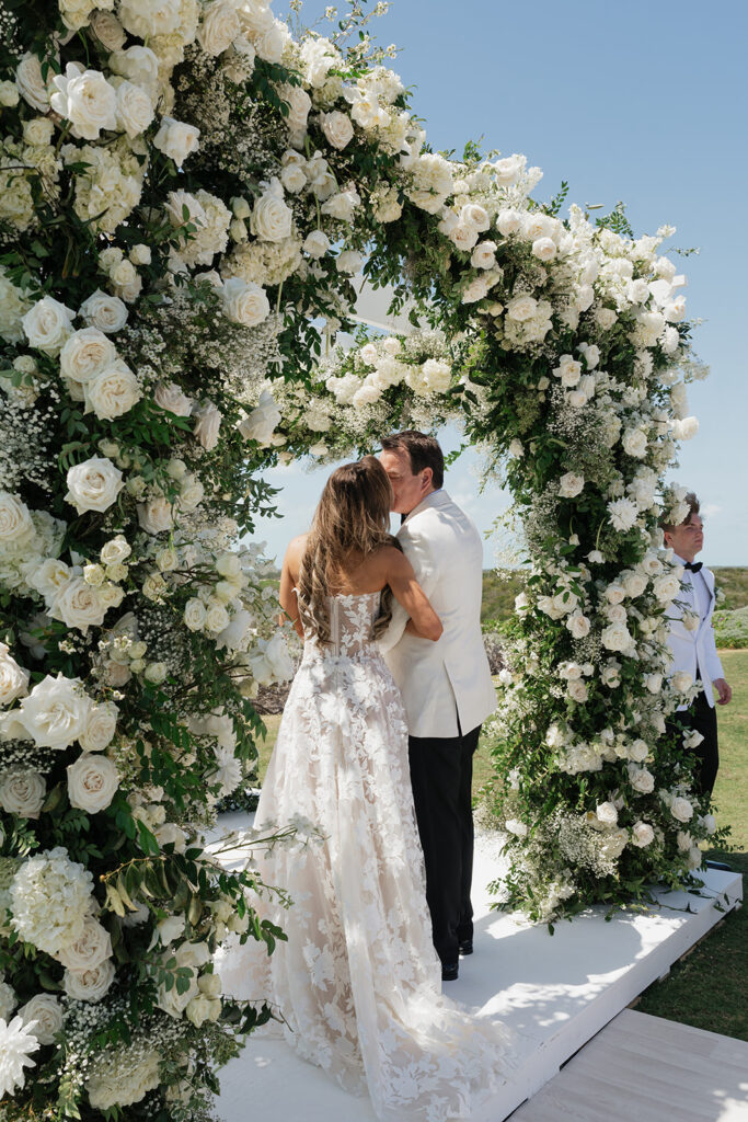 Lush and romantic ceremony chuppah florals for beachfront wedding in the Bahamas. The chuppah highlights garden roses, hydrangeas, delphinium, spray roses, baby’s breath, chrysanthemums, oncidium, wisteria, tulips and a mixture of airy greens to create an elegant and dramatic focal point. Layered textures and soft movement blend seamlessly with lush aisle meadows featuring the same flowers as the chuppah. Design by Rosemary & Finch Floral Design in Nashville, TN.
