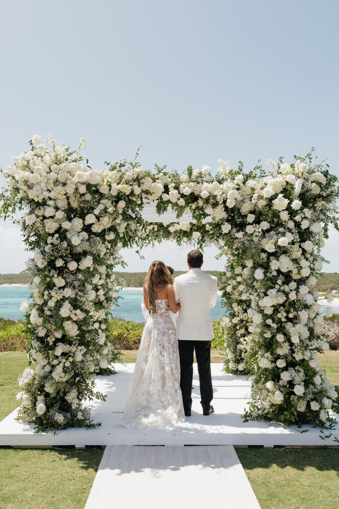Lush and romantic ceremony chuppah florals for beachfront wedding in the Bahamas. The chuppah highlights garden roses, hydrangeas, delphinium, spray roses, baby’s breath, chrysanthemums, oncidium, wisteria, tulips and a mixture of airy greens to create an elegant and dramatic focal point. Layered textures and soft movement blend seamlessly with lush aisle meadows featuring the same flowers as the chuppah. Design by Rosemary & Finch Floral Design in Nashville, TN.