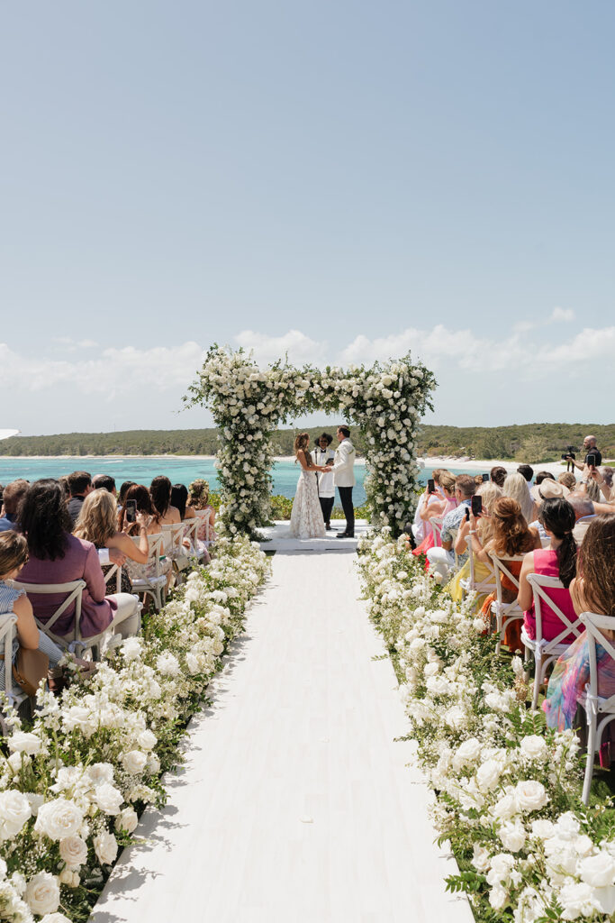 Lush and romantic ceremony chuppah florals for beachfront wedding in the Bahamas. The chuppah highlights garden roses, hydrangeas, delphinium, spray roses, baby’s breath, chrysanthemums, oncidium, wisteria, tulips and a mixture of airy greens to create an elegant and dramatic focal point. Layered textures and soft movement blend seamlessly with lush aisle meadows featuring the same flowers as the chuppah. Design by Rosemary & Finch Floral Design in Nashville, TN.