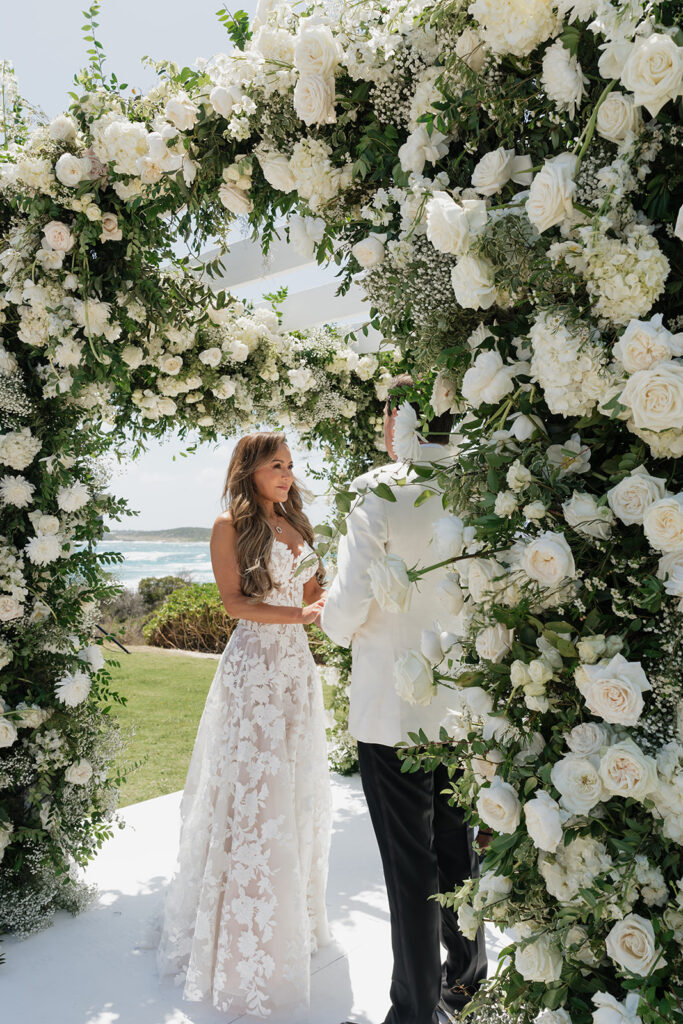 Lush and romantic ceremony chuppah florals for beachfront wedding in the Bahamas. The chuppah highlights garden roses, hydrangeas, delphinium, spray roses, baby’s breath, chrysanthemums, oncidium, wisteria, tulips and a mixture of airy greens to create an elegant and dramatic focal point. Layered textures and soft movement blend seamlessly with lush aisle meadows featuring the same flowers as the chuppah. Design by Rosemary & Finch Floral Design in Nashville, TN.