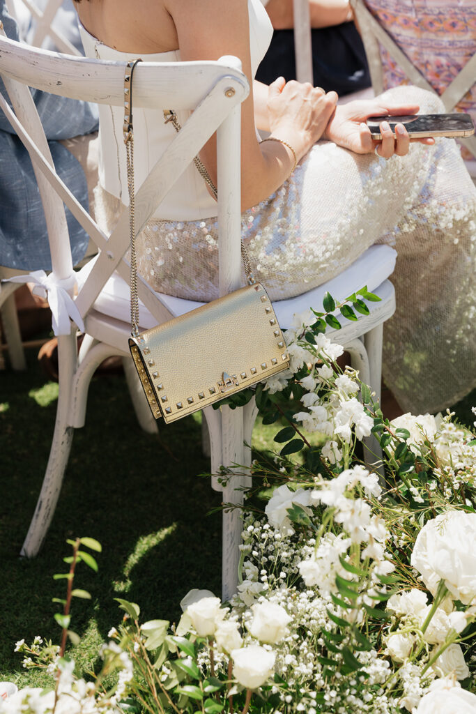 Lush white ceremony florals for a beachfront wedding in the Bahamas featuring garden roses, hydrangeas, delphinium, spray roses, baby’s breath, chrysanthemums, waxflower, carnations, tulips and a mixture of greens to create a refined and romantic aisle arrangement. Layered textures and soft movement give these all-white flowers an elevated, editorial look. Design by Rosemary & Finch Floral Design in Nashville, TN.